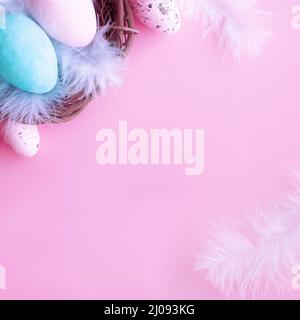 Easter nest with pastel eggs and feathers. Top view on pink background. Stock Photo