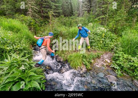 A man helps a girl to jump or ford over a mountain stream on a hike. Travel and outdoors concept Stock Photo