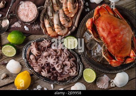 The plates with assorted seafood served with spices on rustic wooden background. Cooked crab, shrimps and baby octopuses for dinner. Seafood concept. Stock Photo