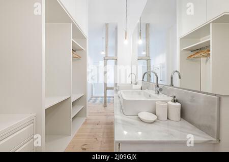 Bathroom of a bedroom with a dressing room with a white marble top with gray veining, a double white porcelain sink, a large long mirror and a shower Stock Photo