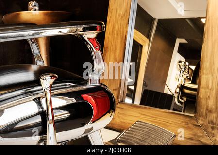 black leather armchairs with chrome in front of rectangular mirrors with gold frame in men's beauty salon Stock Photo
