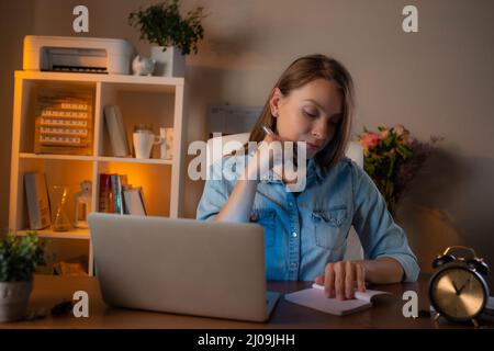 Young woman working at her workplace at office, use laptop and makes notes. Concept of working moments. Stock Photo