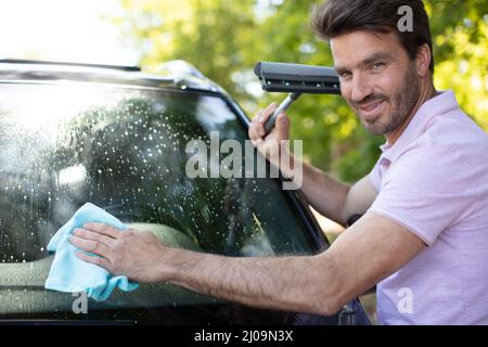 happy man holding squeegee while cleaning car window Stock Photo