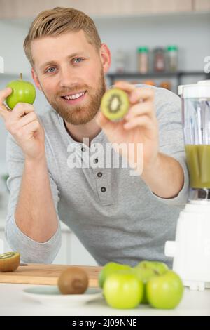 happy man making juice or smoothie in kitchen Stock Photo