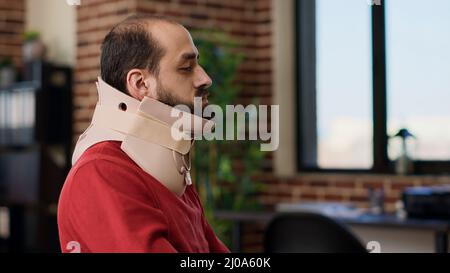 Businessman wearing cervical neck collar at e commerce job, after injury accident. Young person with medical foam working on financial strategy, recovering after vertebrae fracture at desk. Stock Photo
