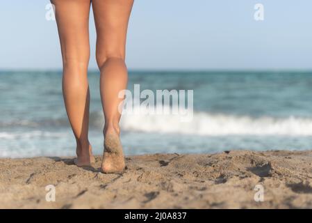 Crop female walking on sandy beach in sunny day Stock Photo