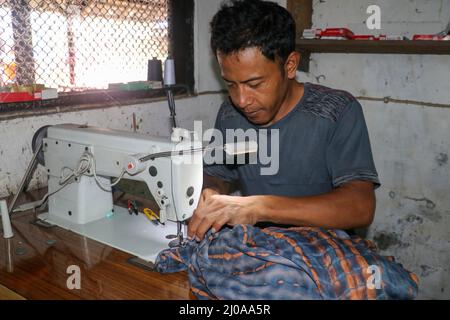 Asian man sews clothes on a sewing machine. Middle aged male tailor working with sewing machine and cloth in workshop Stock Photo