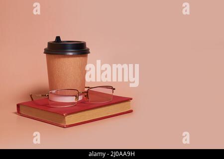 A paper cup of coffee and glasses lie on a book on a colored background Stock Photo