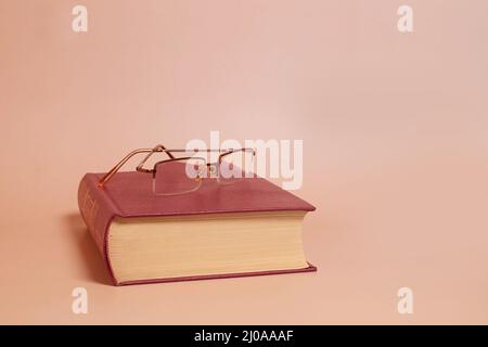 Reading glasses lie on a thick book, colored background. Side view Stock Photo