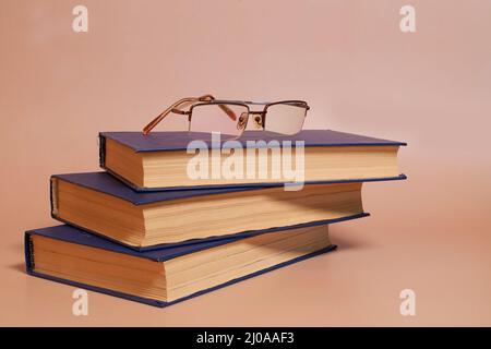 Reading glasses are on a stack of books on a colored background. Side view Stock Photo