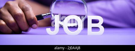 Person's Hand Looking At Job Through Magnifying Glass On Desk Stock Photo