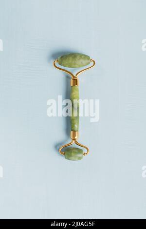 Green jade face roller on light blue background. Massage tool for facial skin care, SPA self and beauty care treatment concept. Stock Photo