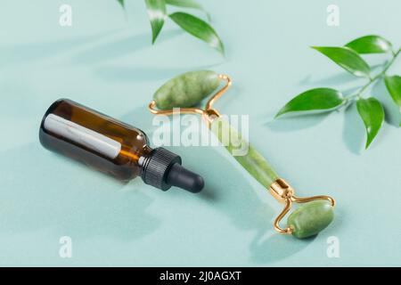 Green jade face roller, anti age treatment and green leaves on light blue background. Massage tool for facial skin care, SPA self and beauty care trea Stock Photo