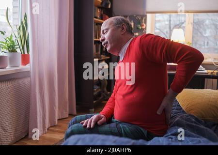 Senior man suffering from pain in back or reins at home sitting on bed. Stock Photo