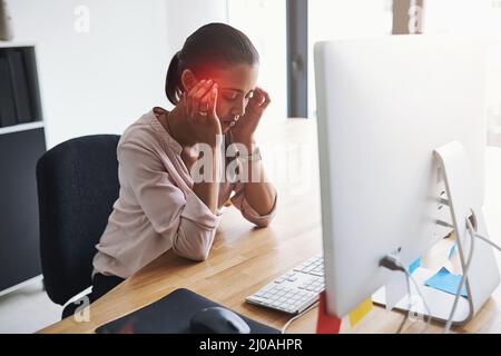 The stress and anxiety of work can trigger severe headaches. Shot of a young businesswoman suffering with a headache while working in an office. Stock Photo