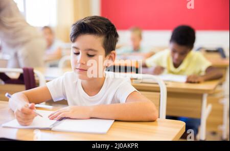 Focused tween boy writing exercises in classroom during lesson Stock Photo