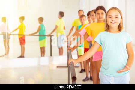 Smiling tween girl practicing classic dance moves near ballet barre Stock Photo