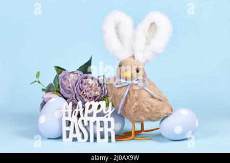 Easter chick with bunny ears, painted eggs and text 'Happy Easter' on blue background Stock Photo