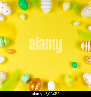 Easter frame with eggs and feathers on a yellow background. View from above. Card with copy space for text. Stock Photo