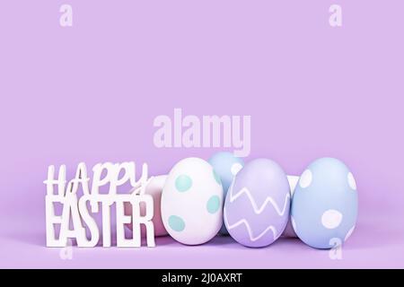 Pastel colored easter eggs and text 'Happy Easter' on violet background with copy space Stock Photo