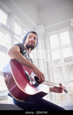 Mastering his musical skills. Cropped shot of a handsome young man playing a guitar at home. Stock Photo