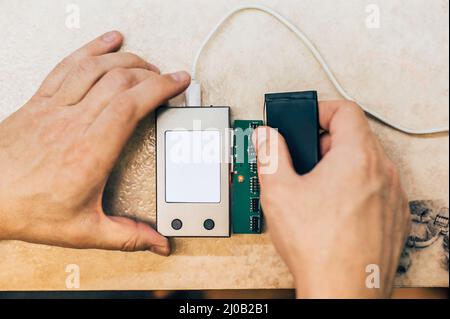 Technician testing and analyzing faulty mobile phone battery in electronic smartphone technology service. Cellphone technology device maintenance engi Stock Photo