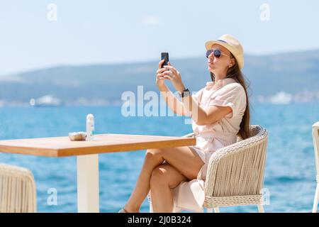 Young lady in dress sitting at the table in cafe near the sea Stock Photo