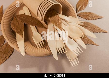 Eco-friendly disposable utensils made of bamboo wood and paper on a light beige background. Fork, knives, plates, paper cups and dry leaves Stock Photo