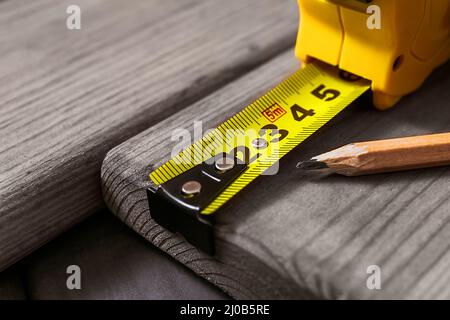 Hands in gloves of joiner in carpentry. Carpenter is measuring length of wood planks or timbers by measuring tape or ruler. Carpenter workspace, craft Stock Photo