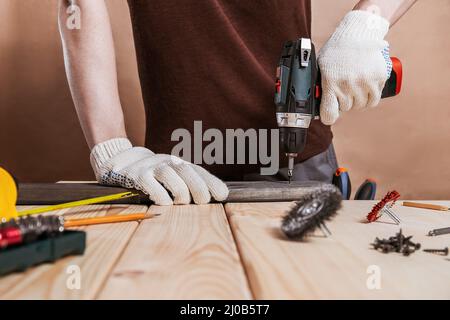 Close up portrait and details of caucasian male worker using electric screwdriver instrument in hand and repairing new wooden desk, home improvement c Stock Photo