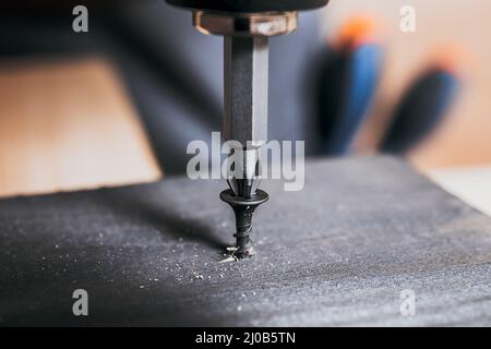 Screw screwed into timber wood on wooden top table background. Electric Screwdriver or drill screwing screw, nail or bolt into wooden planks. Repair Stock Photo