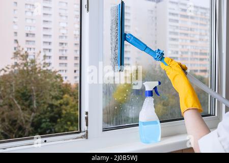 Man in yellow rubber gloves cleaning window with cleaner spray detergent and squeegee or rag at home or office, copy space. Housework and housekeeping Stock Photo