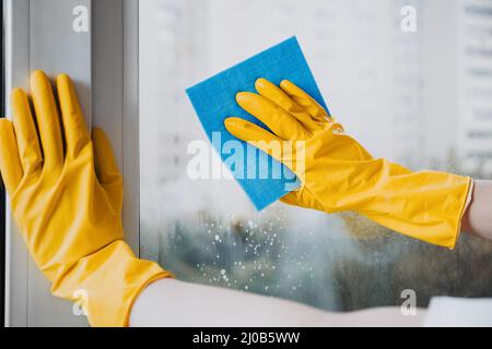 Man in yellow rubber gloves cleaning window with cleaner spray detergent and squeegee or rag at home or office, copy space. Housework and housekeeping Stock Photo