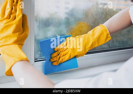Man in yellow rubber gloves cleaning window glasse with cleaner spray detergent and squeegee or rag at home or office, copy space. Housework and house Stock Photo