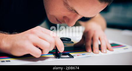 Worker in a printing and press centar uses a magnifying glass and check the print quality Stock Photo