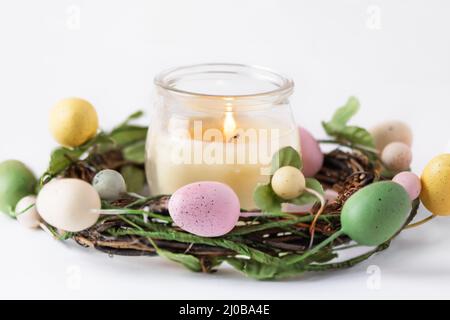 Candle in decorative easter wreath with colourful Easter eggs over white background. Happy Easter greeting card. Stock Photo