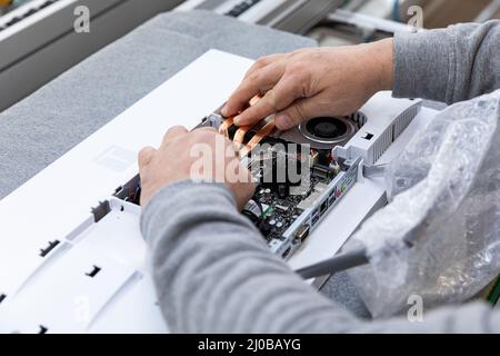 Minsk, Belarus - Dec 15, 2021: Photo of hands of a man who assembles a computer monitor system block on an conveyor belt at a monoblock assembly plant Stock Photo