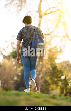 Young man with a bag walking around the park with some trees on the background Stock Photo