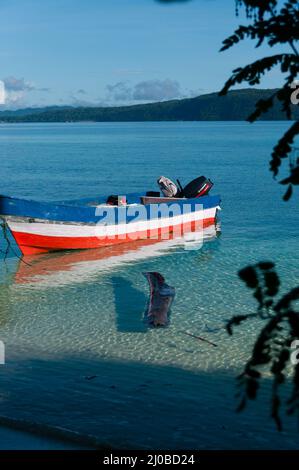 Small wooden boat in shallow clear water tied up by the white sand beach Stock Photo