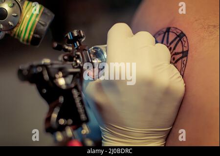 Master tattoo draws the blue paint on the clients tattoo Stock Photo