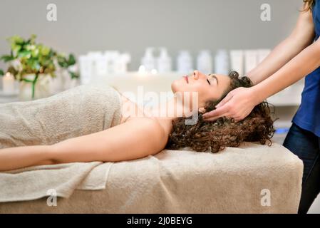 Side view of serene female client with closed eyes wrapped in towel lying on couch and enjoying massage in beauty salon during relaxing procedure Stock Photo