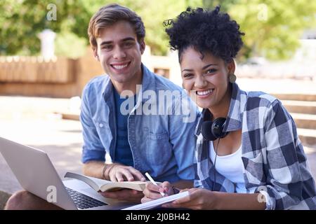 Studying together has helped our relationship grow. Shot of two college students studying together on campus grounds. Stock Photo