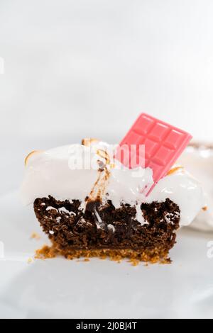 Sliced s'mores cupcakes with meringue frosting and garnished with star-shaped chocolate graham cracker and a mini pink chocolate bar on a white plate. Stock Photo