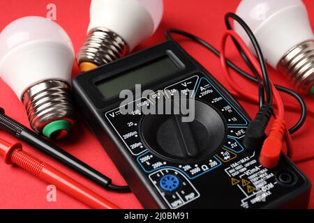 Multimeter and energy saving bulbs on red background Stock Photo