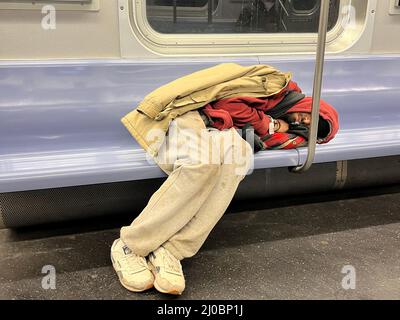 Tired young man sprawled out on a subway seat in on a train going through Manhattan. Stock Photo