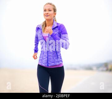 Getting fitter by the step. Shot of a young woman in sportswear standing at the beach. Stock Photo