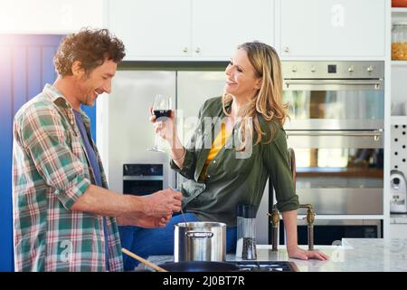 Catching up after work. Shot of a happy mature couple enjoying some wine while preparing a meal together at home. Stock Photo