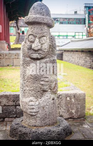 Stone idol (Dolharubang, the grandfather stones) at front of Jeju Mokgwana, the oldest remaining building in Jeju for former cen Stock Photo