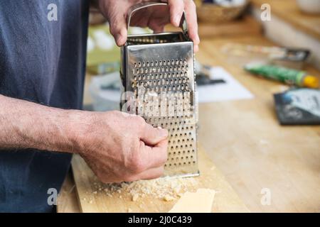 Hands of a man grating parmesan cheese on a metal grater on a wooden kitchen counter, cooking at home, copy space, selected focus, narrow depth of fie Stock Photo