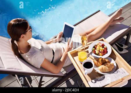 She makes sure to take a vacation every year. An attractive young woman enjoying her breakfast poolside. Stock Photo